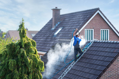 Cleaner with pressure washer at roof of house cleaning the roof tiles